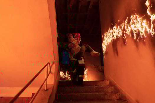Brave Fireman Descends Stairs of a Burning Building and Holds Saved Girl in His Arms. Open fire and one Firefighter in the Background. photo