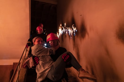 Brave Fireman Descends Stairs of a Burning Building and Holds Saved Girl in His Arms. Open fire and one Firefighter in the Background. photo