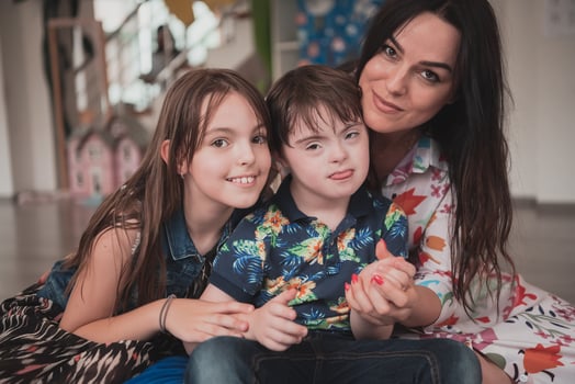 A girl and a woman hug a child with down syndrome in a modern preschool institution photo