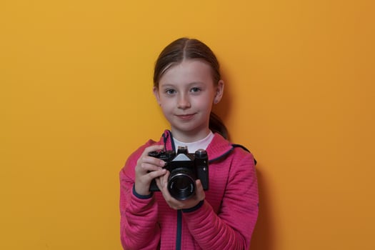 Little girl photographer isolated on yellow background smiling taking photos with a retro vintage camera.