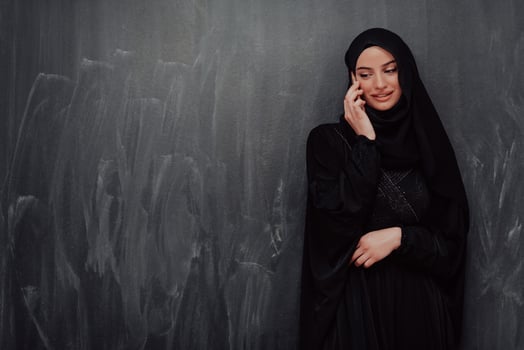 Young modern muslim business woman using smartphone wearing hijab clothes in front of black chalkboard photo