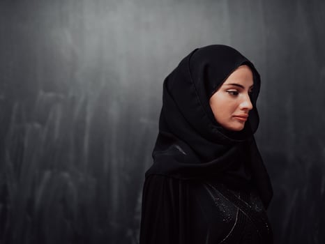 Portrait of beautiful muslim woman in fashionable dress with hijab in front of black chalkboard representing modern islam fashion and ramadan kareem concept photo