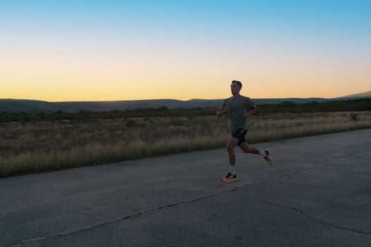 Attractive fit man running fast along countryside road at sunset light, doing jogging workout outdoors photo