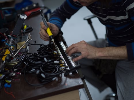 Industrial worker man soldering cables of manufacturing equipment in a factory. Selective focus photo