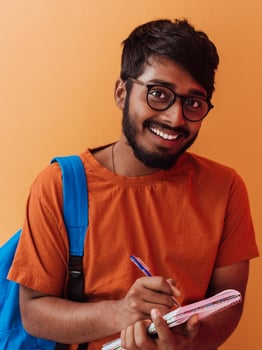 Indian student with blue backpack, glasses and notebook posing on orange background. The concept of education and schooling. Time to go back to school photo