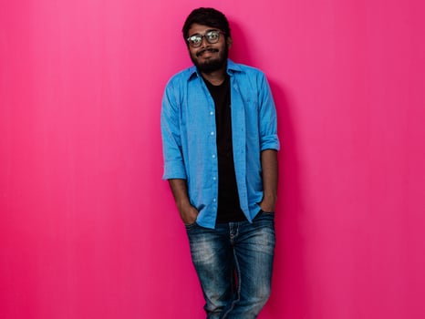 Indian smiling young man with blue shirt and glasses posing on pink background photo