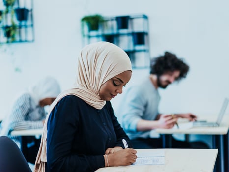 Photo of an African American Muslim woman being educated about business development in a modern classroom