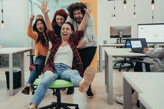 Team building and office fun. Young cheerful businesspeople in smart casual wear having fun while racing on office chairs and smiling. photo