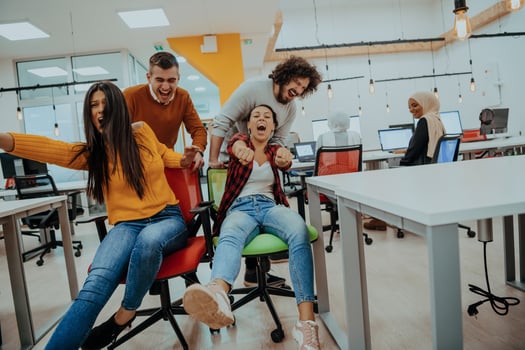 Team building and office fun. Young cheerful businesspeople in smart casual wear having fun while racing on office chairs and smiling. photo