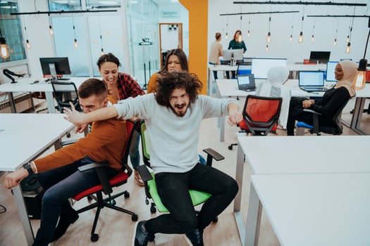 Team building and office fun. Young cheerful businesspeople in smart casual wear having fun while racing on office chairs and smiling. photo