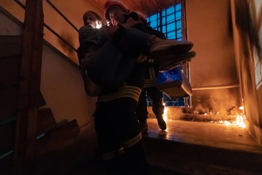 Brave Fireman Descends Stairs of a Burning Building and Holds Saved Girl in His Arms. Open fire and one Firefighter in the Background. photo