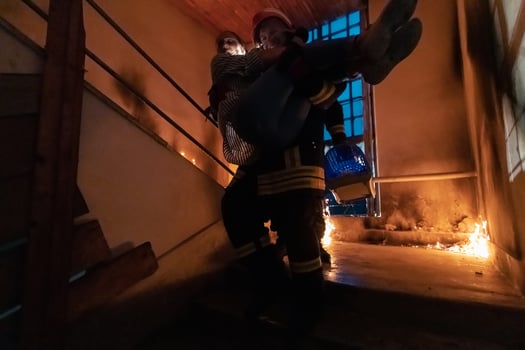 Brave Fireman Descends Stairs of a Burning Building and Holds Saved Girl in His Arms. Open fire and one Firefighter in the Background. photo