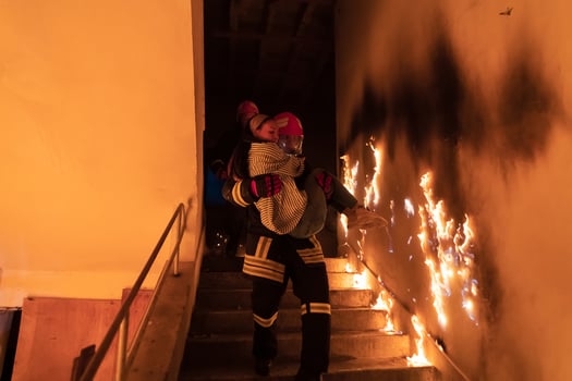 Brave Fireman Descends Stairs of a Burning Building and Holds Saved Girl in His Arms. Open fire and one Firefighter in the Background. photo