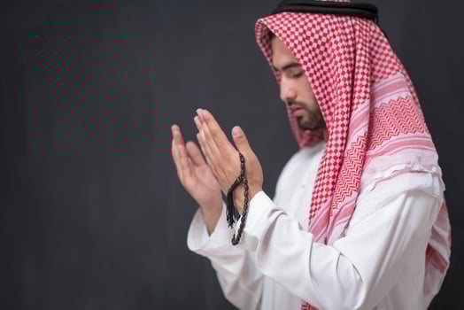 A young Arabian man in traditional clothes making a traditional prayer to God keeps his hands in praying gesture in front of a black background photo
