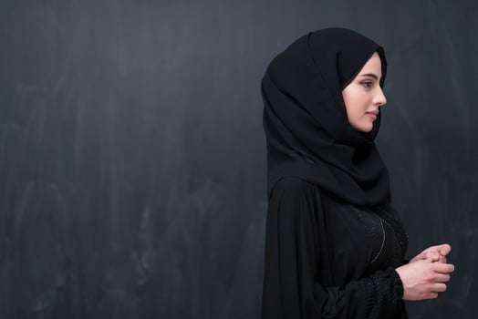 Portrait of beautiful muslim woman in fashionable dress with hijab in front of black chalkboard representing modern islam fashion and ramadan kareem concept photo