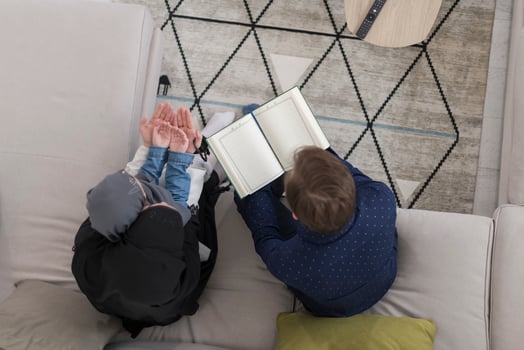 Top view photo of traditional muslim family parents with children reading Quran and praying together