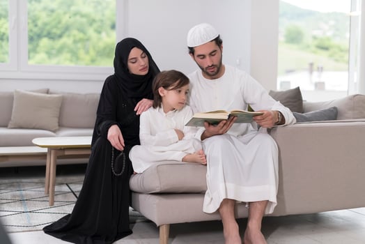 Traditional muslim family parents with children reading Quran and praying together on the sofa before iftar dinner during a ramadan feast at home photo