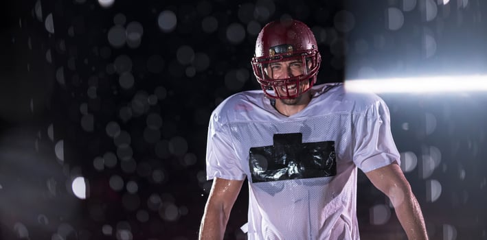 American Football Field Lonely Athlete Warrior Standing on a Field Holds his Helmet and Ready to Play. Player Preparing to Run, Attack and Score Touchdown. Rainy Night with Dramatic Fog, Blue Light photo