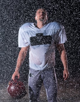American Football Field Lonely Athlete Warrior Standing on a Field Holds his Helmet and Ready to Play. Player Preparing to Run, Attack and Score Touchdown. Rainy Night with Dramatic Fog, Blue Light photo