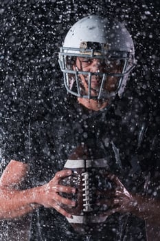 American Football Field Lonely Athlete Warrior Standing on a Field Holds his Helmet and Ready to Play. Player Preparing to Run, Attack and Score Touchdown. Rainy Night with Dramatic Fog, Blue Light photo