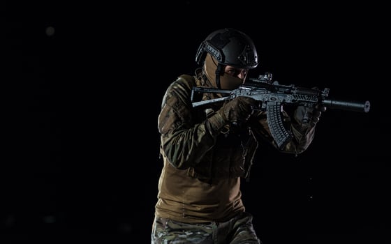 Army soldier in Combat Uniforms with an assault rifle, plate carrier and combat helmet going on a dangerous mission on a rainy night. photo