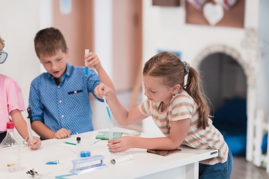 Elementary School Science Classroom Enthusiastic Teacher Explains Chemistry to Diverse Group of Children, Little Boy Mixes Chemicals in Beakers. Children Learn with Interest photo