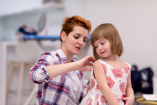 mother helping daughter while putting on a dress photo