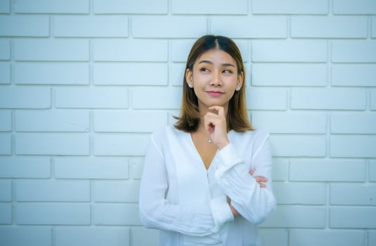Beautiful asian business woman is standing in a thoughtful pose at the copy space with a white brick background, Digital marketing. photo