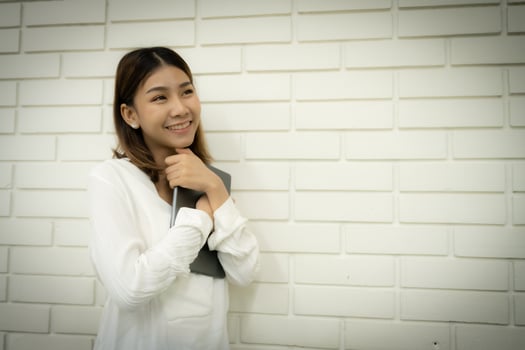 Beautiful asian online seller feeling happy after her store's followers have increased she hugged the tablet and looking to the copy space with a smiling face against a white brick wall background. photo