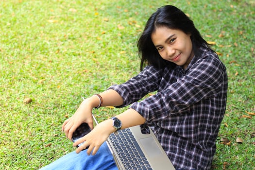 excited beautiful asian student using laptop and smartphone and reading book to studying and planning her work photo