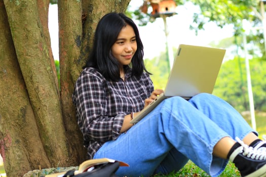 happy asian student using laptop and reading book to study for exam and surfing in the internet with excitement photo