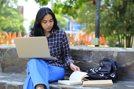 portrait of focused young asian woman surfing internet using laptop to working remotely, read book, and writing in notebook. attractive asian student study in outdoors photo