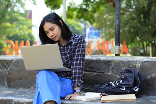 portrait of focused young asian woman surfing internet using laptop to working remotely, read book, and writing in notebook. attractive asian student study in outdoors photo