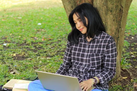 young smiling asian woman using laptop and writing notebook, cheerful asian student watching webinar and studying from e course photo