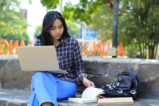 portrait of focused young asian woman surfing internet using laptop to working remotely, read book, and writing in notebook. attractive asian student study in outdoors photo