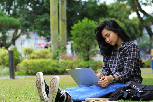 portrait of focused young asian woman surfing internet using laptop to working remotely, read book, and writing in notebook. attractive asian student study in outdoors photo