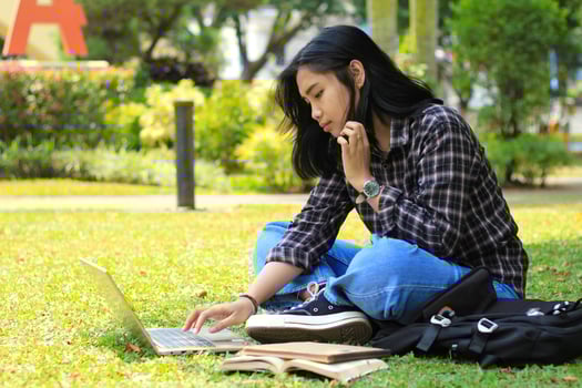 portrait of focused young asian woman surfing internet using laptop to working remotely, read book, and writing in notebook. attractive asian student study in outdoors photo