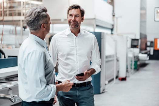 Mature businessman holding smart phone while discussing with colleague in industry photo