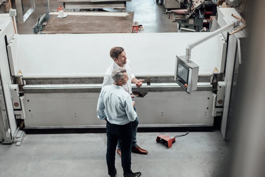 Mature male engineers discussing over manufacturing equipment in factory photo