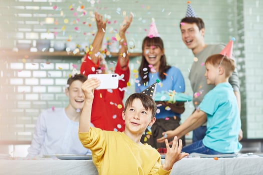 Mother and sons celebrating grandmother's bithday in their kitchen, boy taking selfies photo