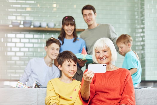 Mother and sons celebrating grandmother's bithday in their kitchen, boy taking selfies photo