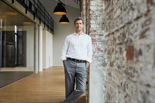 Portrait of confident businessman leaning against brick wall in modern office photo