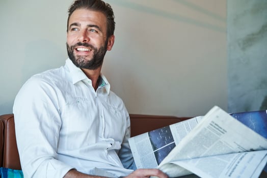 Portrait of happy businessman wearing white shirt sitting on couch with newspaper photo