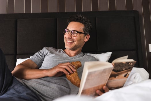 Happy man lying in bed at home with croissant and book photo