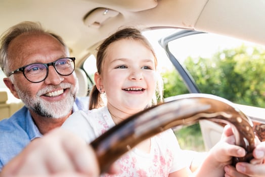 Little girl sitting on lap of grandfather, pretending to steer the car photo