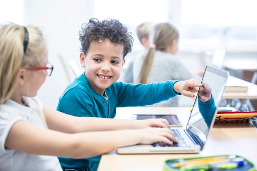 Schoolboy and schoolgirl using laptop together in class photo
