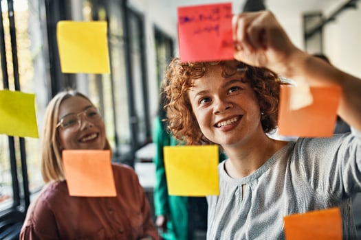 Happy colleagues with sticky notes at glass pane in office photo
