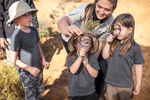 Children with teacher examining plant with magnifying glass photo