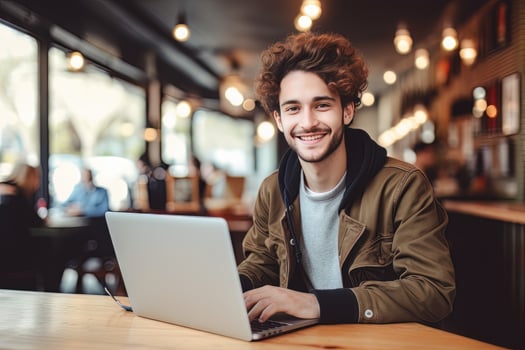 Portrait of Cheerful Male Student Learning Online in Coffee Shop, Young European Man Studies with Laptop in Cafe, Doing Homework photo
