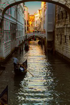 Several gondolas sail in a row along the narrow venetian canal in the light of the setting sun. photo